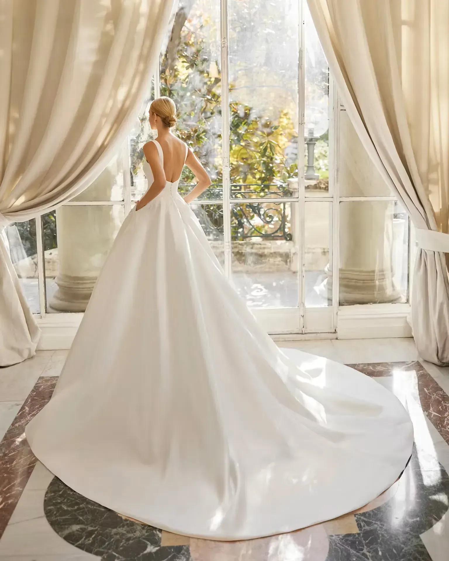 Una mujer con un vestido de novia blanco está parada frente a una ventana.