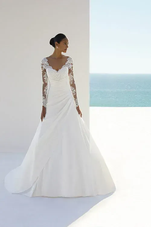 Una mujer lleva un vestido de novia blanco con mangas largas.