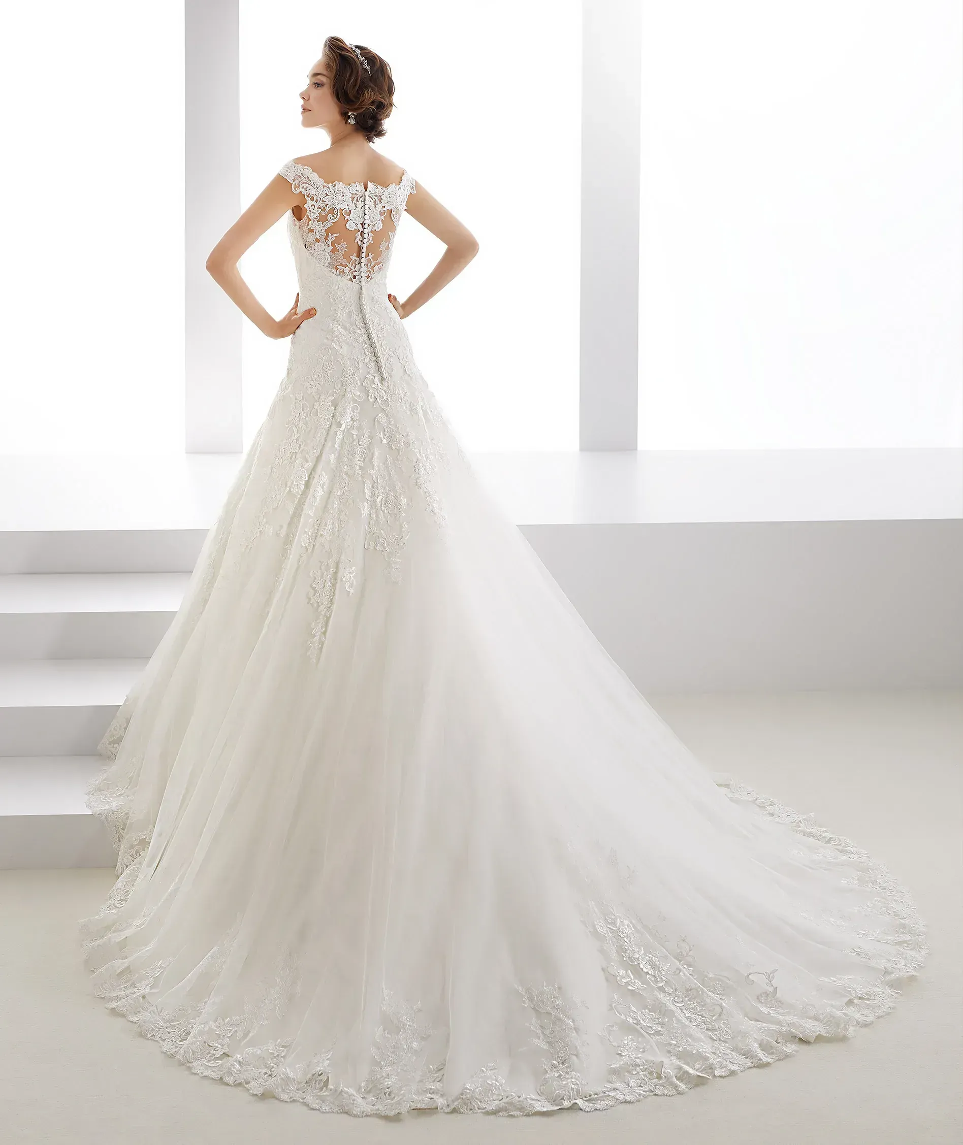 Una mujer lleva un vestido de novia blanco con una larga cola.