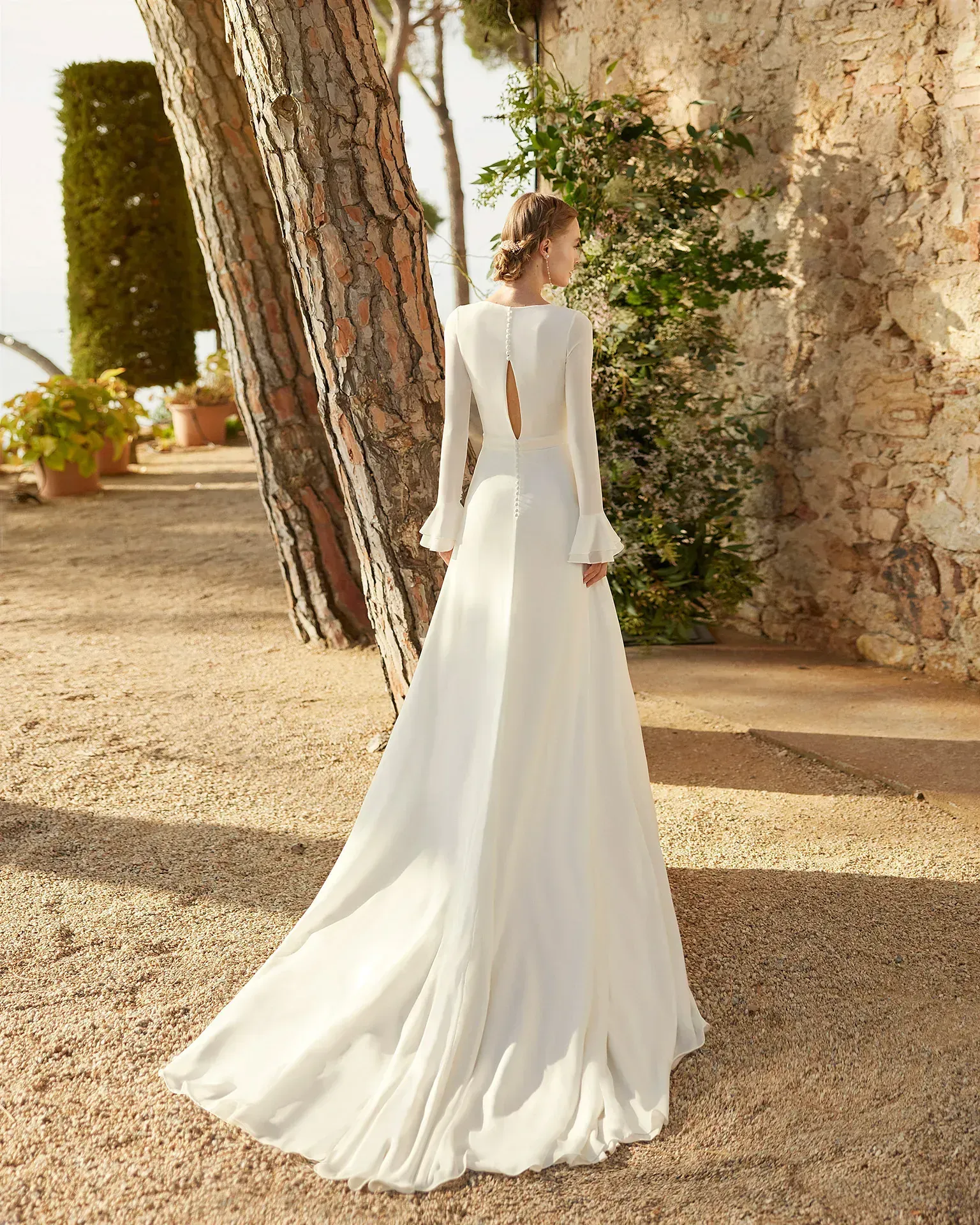 Una mujer con un vestido blanco está de pie junto a un árbol.