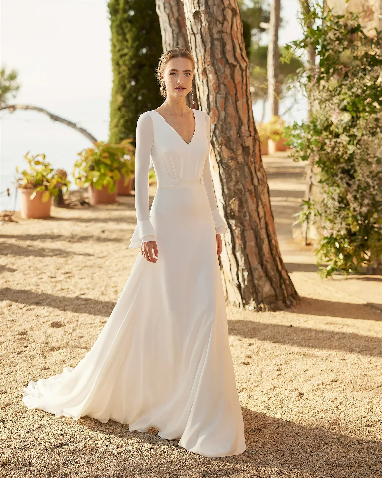 Una mujer con un vestido de novia blanco está de pie junto a un árbol.
