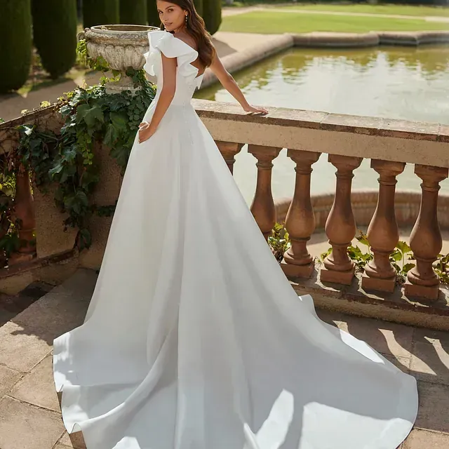 Una mujer con un vestido de novia blanco está de pie junto a una fuente.