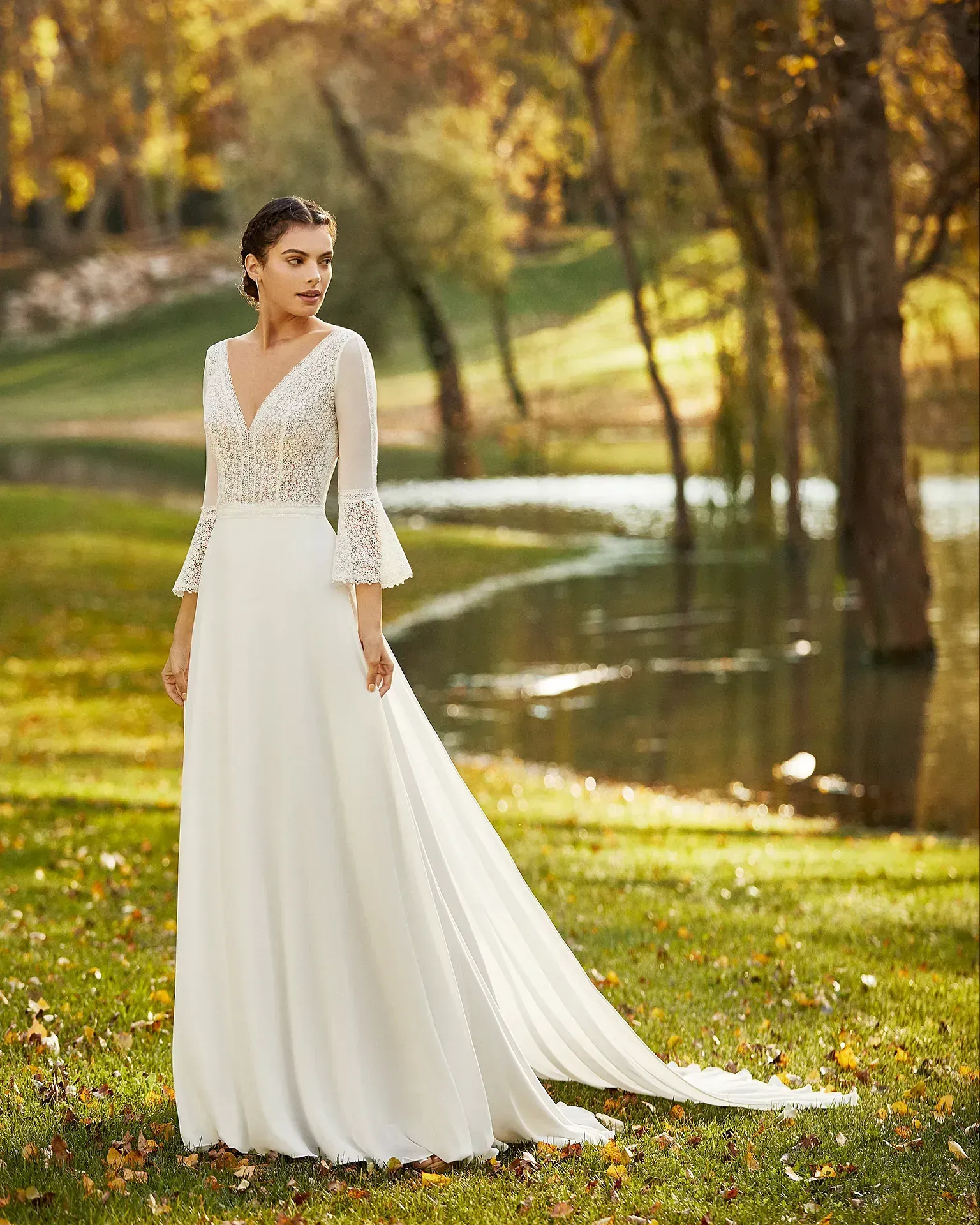 Una mujer con un vestido de novia blanco está parada en el césped cerca de un lago.
