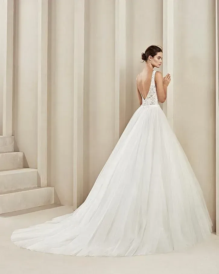 Una mujer con un vestido de novia blanco está de pie junto a una pared.