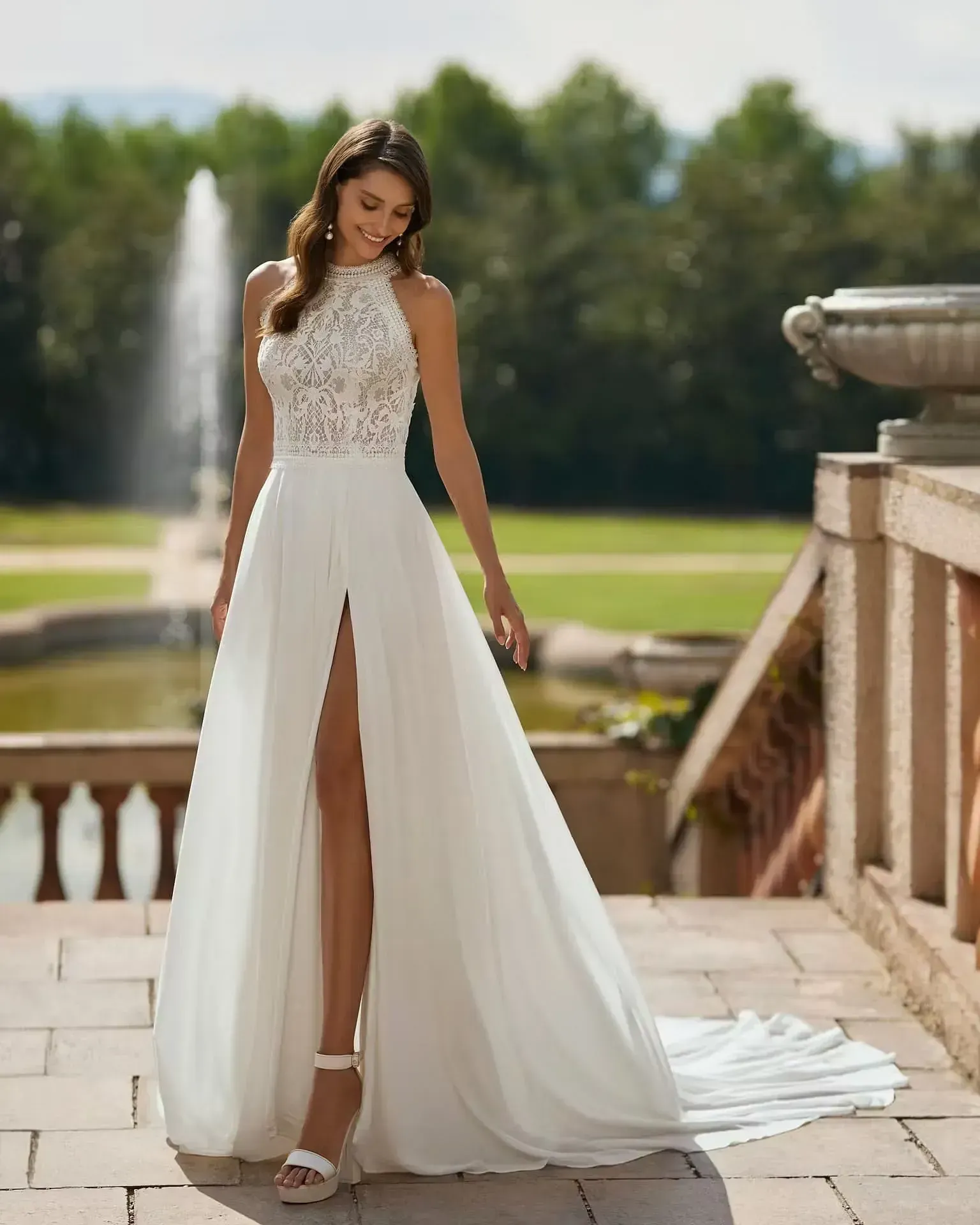 Una mujer con un vestido de novia blanco está parada frente a una fuente.