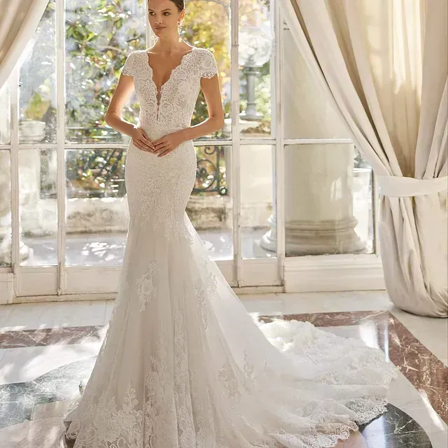 Una mujer con un vestido de novia blanco está parada frente a una ventana.