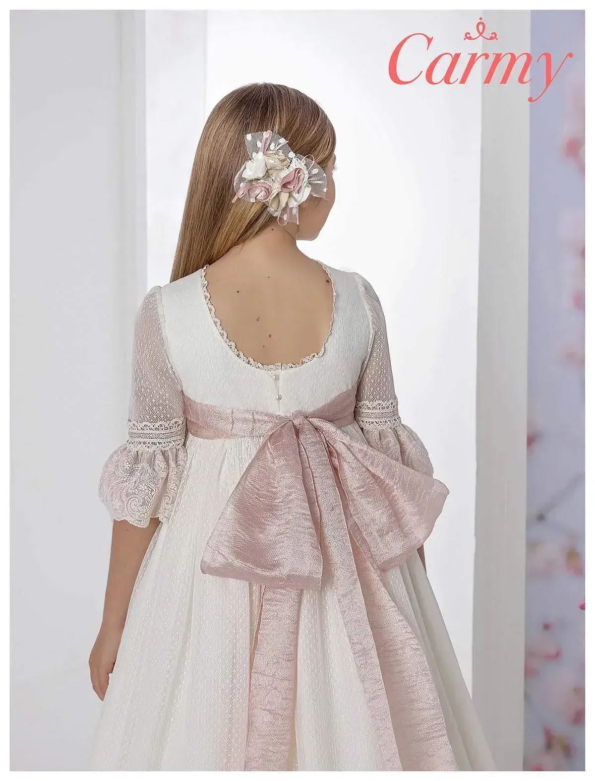 La espalda de una niña con un vestido blanco con un lazo rosa.