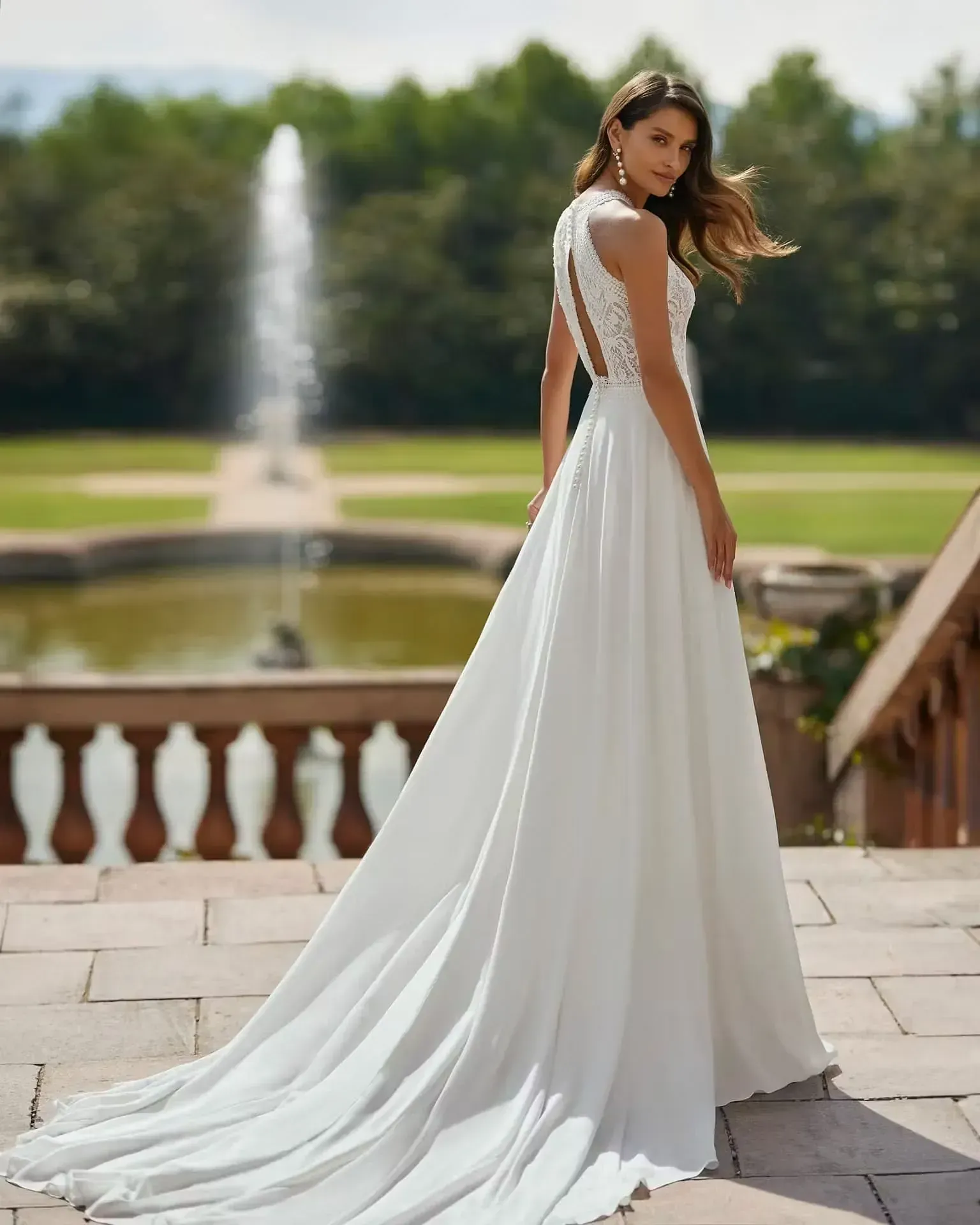 Una mujer con un vestido de novia blanco está parada frente a una fuente.