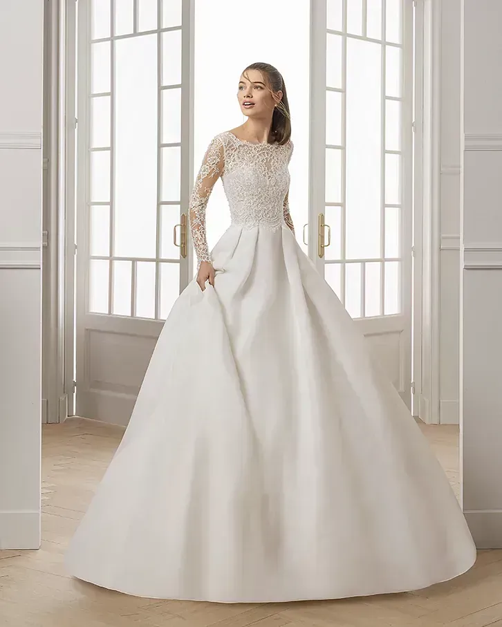 Una mujer lleva un vestido de novia blanco con mangas largas.