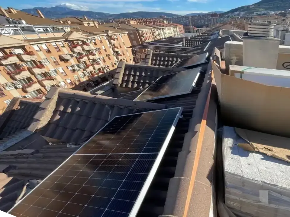 Paneles solares sobre un tejado de tejas con edificios urbanos al fondo y una montaña cubierta de nieve.