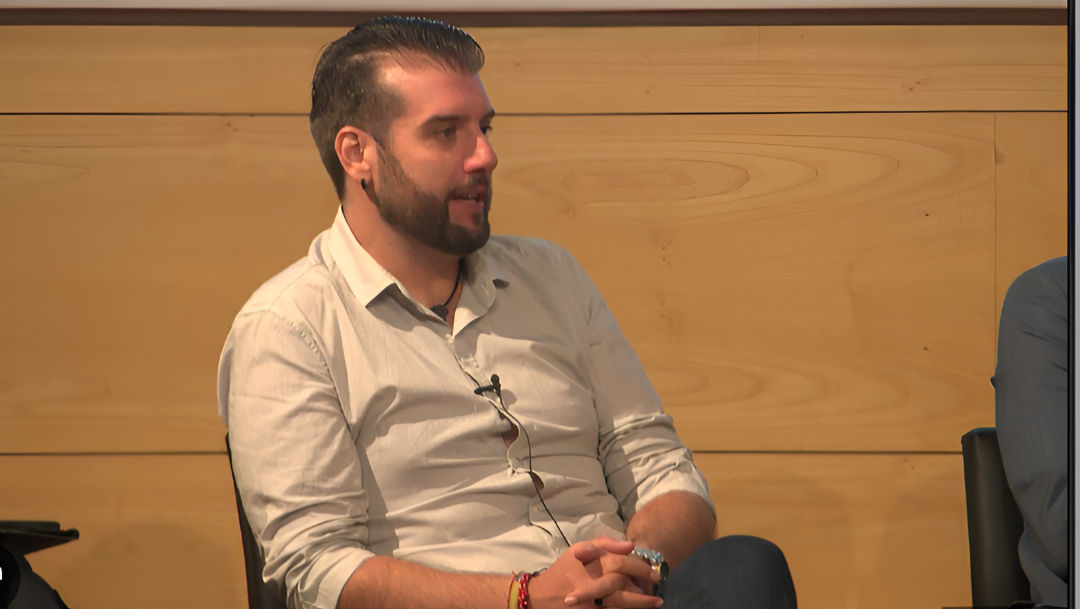 Sitio de construcción cercado en un estacionamiento pavimentado con montones de escombros, vehículos y un cielo despejado.