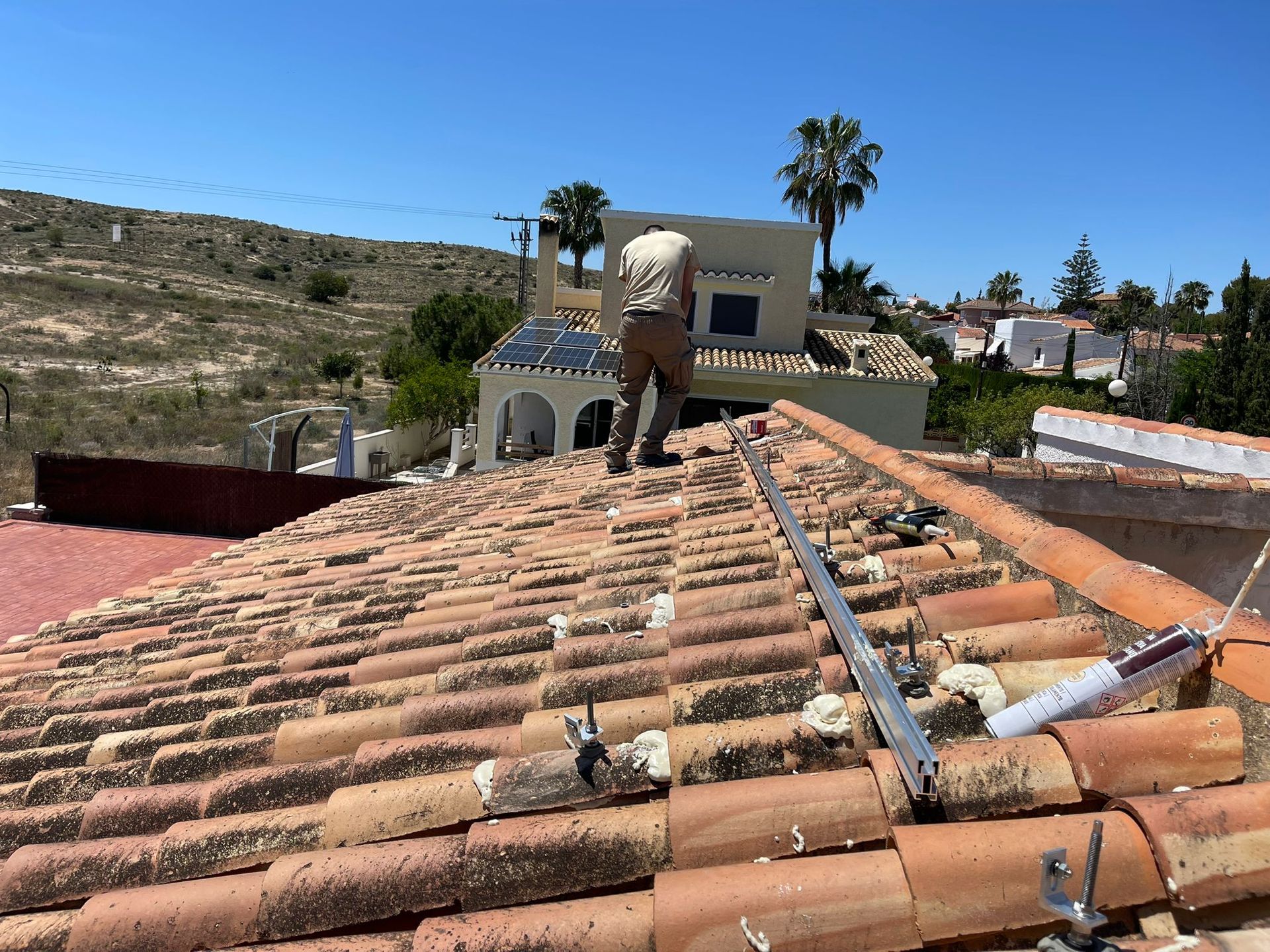 Persona instalando paneles solares en un techo de tejas bajo un cielo soleado.