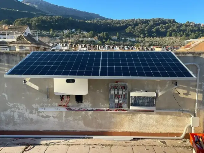 Instalación de paneles solares en un tejado con componentes eléctricos conectados; día soleado, fondo de montañas.