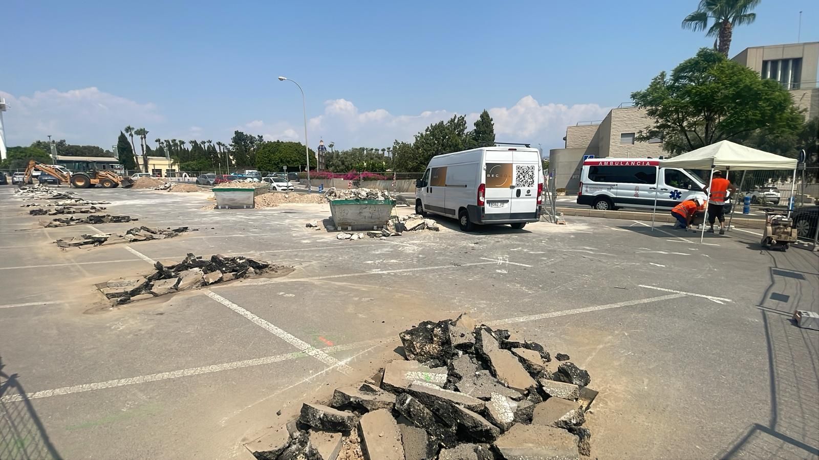 Estacionamiento en construcción; escombros, camionetas, trabajadores, cielo azul.