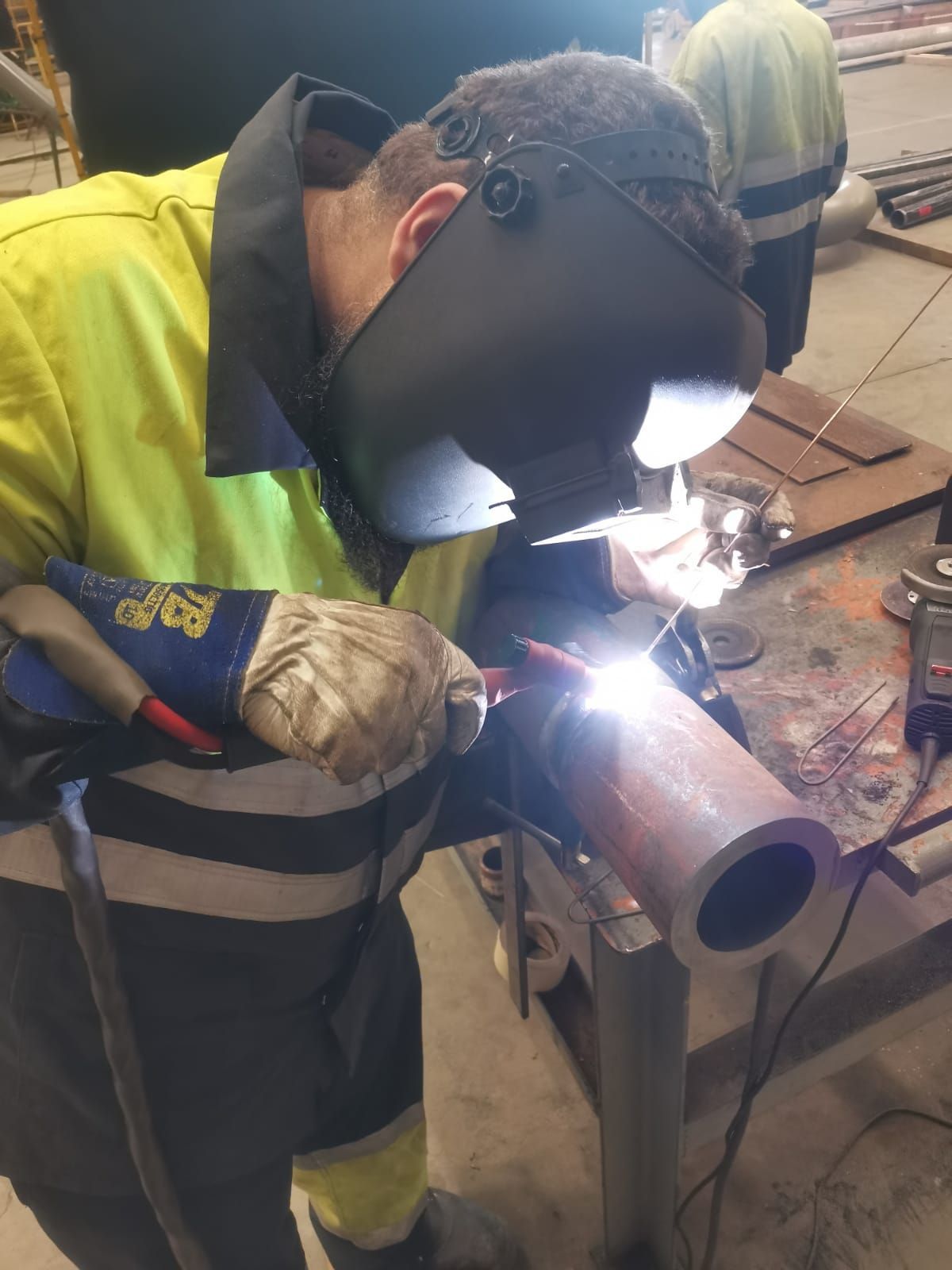 Sitio de construcción cercado en un estacionamiento pavimentado con montones de escombros, vehículos y un cielo despejado.