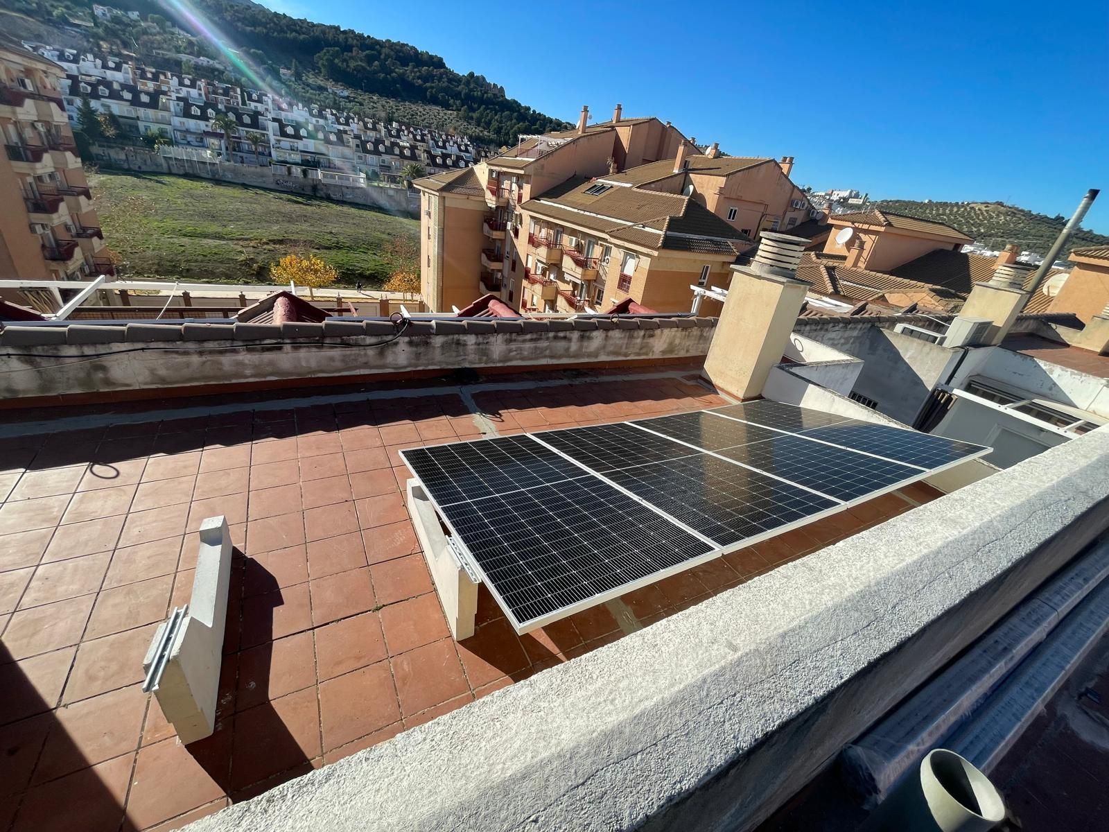 Instalación de paneles solares en un tejado con componentes eléctricos conectados; día soleado, fondo de montañas.