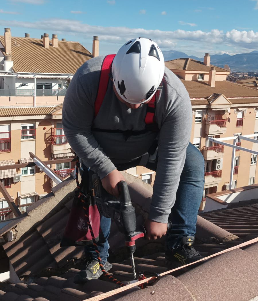 Persona instalando paneles solares en un techo de tejas bajo un cielo soleado.