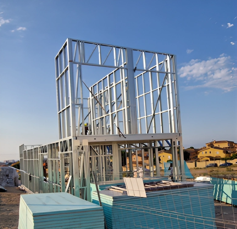 Sitio de construcción: montones de tierra, maquinaria, área de concreto parcialmente construida, autos estacionados, cielo azul.