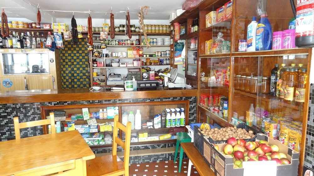 Interior de una pequeña tienda de comestibles bien surtida, con estantes llenos de productos.