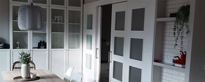 Interior blanco con armarios empotrados, puertas corredizas y mesa de comedor.