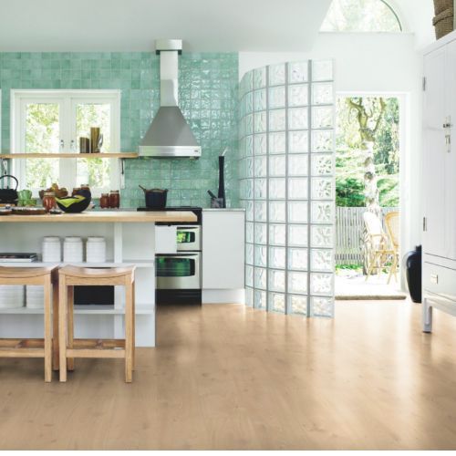 Cocina con piso de madera clara, salpicadero de azulejos turquesa, pared de bloques de vidrio y puerta abierta a un patio.