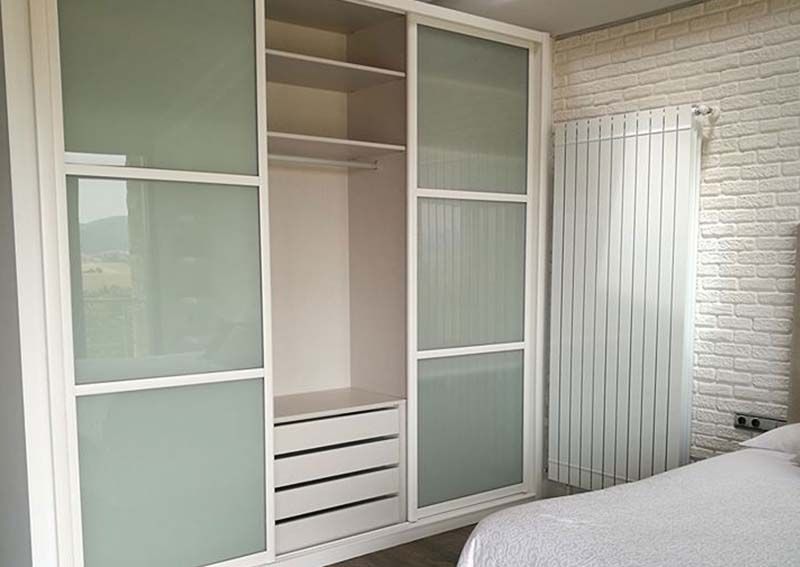 Armario blanco con puertas corredizas de vidrio esmerilado, que se abre para revelar estantes de almacenamiento, cajones y barra para colgar.