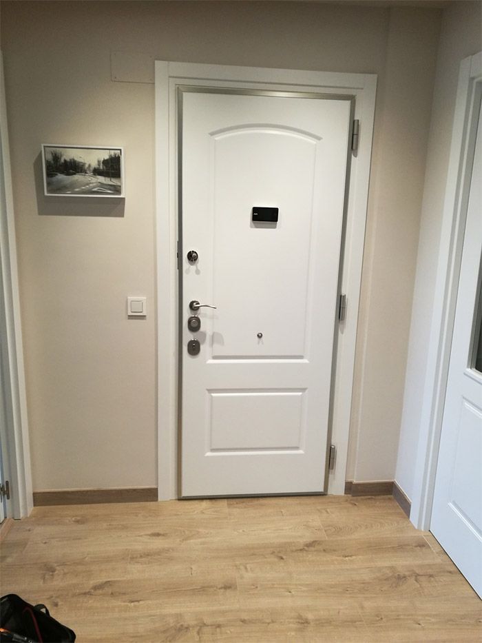 Puerta blanca con herrajes plateados, pequeñas obras de arte y paredes de colores claros en un pasillo.