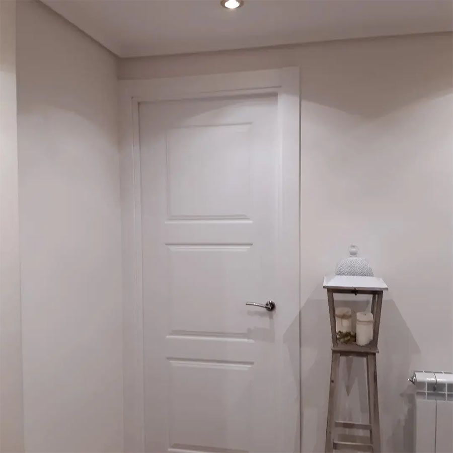 Puerta blanca con tirador plateado y linterna de madera contra una pared blanca.