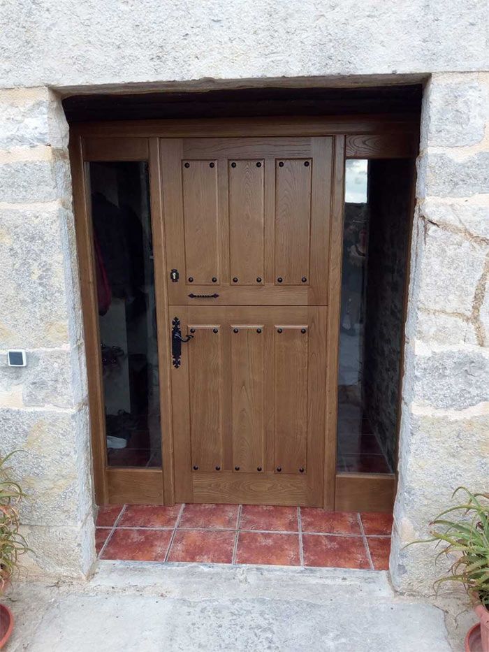 Puerta de madera con ventanas laterales en un portal de piedra. Puerta marrón oscuro con herrajes negros y suelo de baldosas rojas.