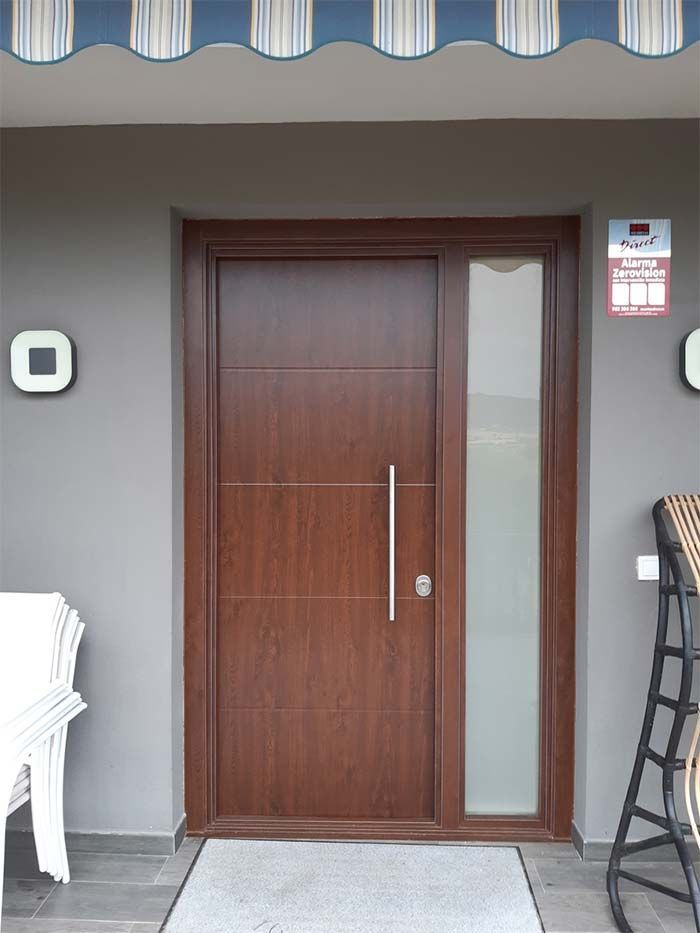 Puerta de madera marrón con panel de vidrio esmerilado y tirador plateado. Paredes grises, alfombra y toldo.