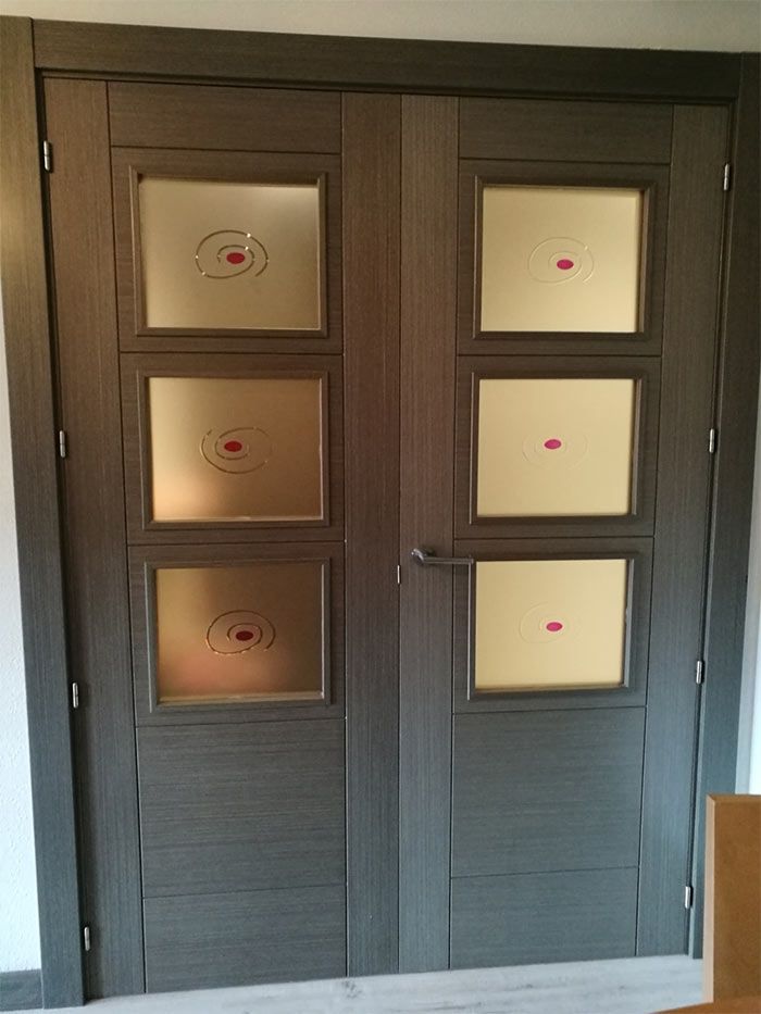 Puertas dobles de color gris oscuro con paneles de vidrio esmerilado, cada una con un diseño de objetivo rojo y una manija plateada.