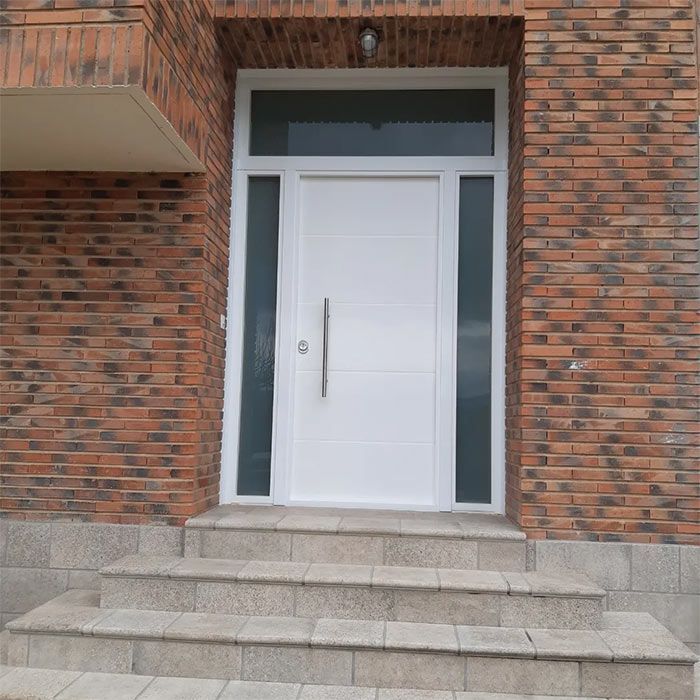 Puerta blanca con ventanales y travesaño, fachada de ladrillo, escalones de granito.