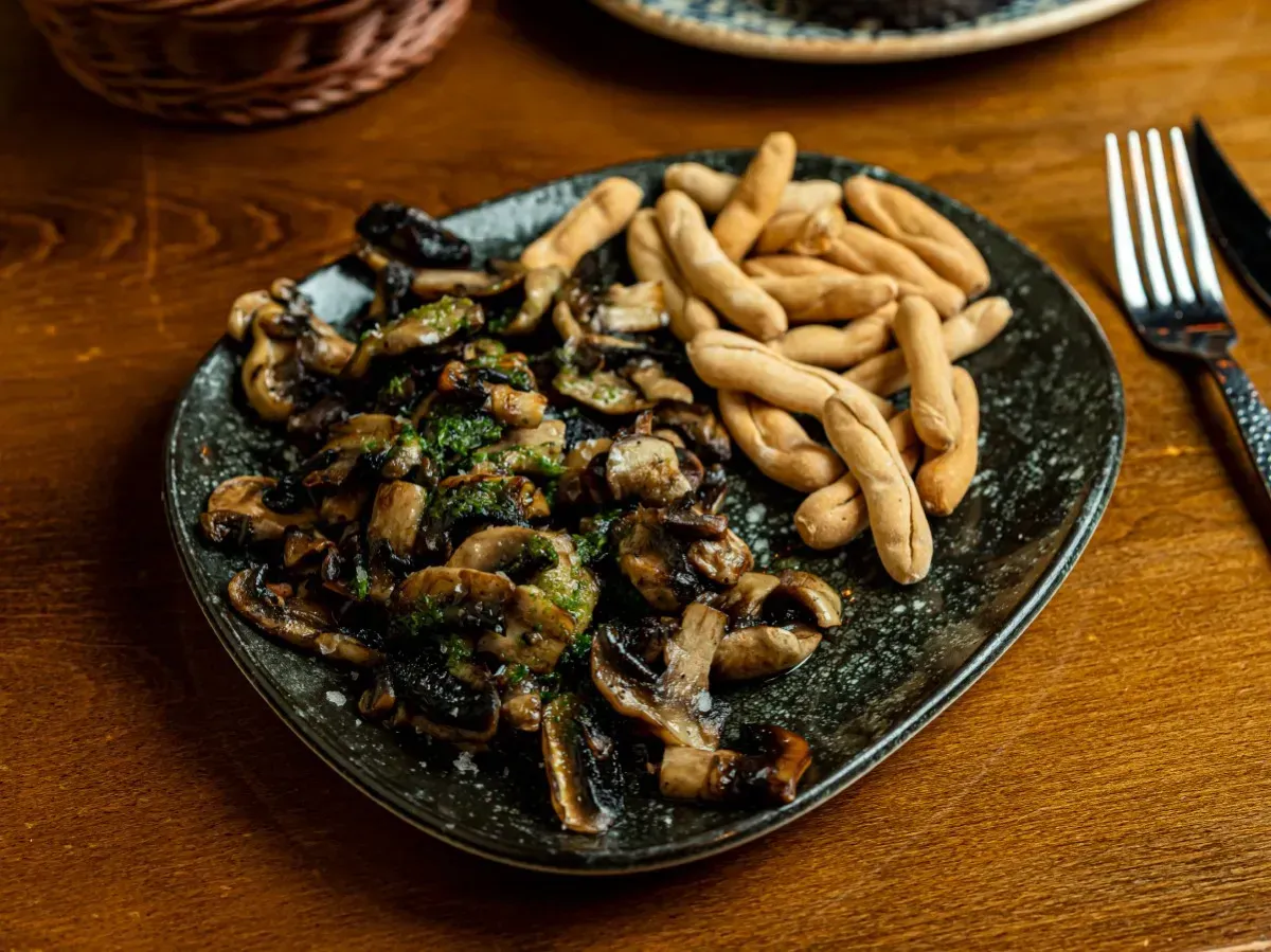 Un plato de comida con champiñones y palitos de pan sobre una mesa de madera.