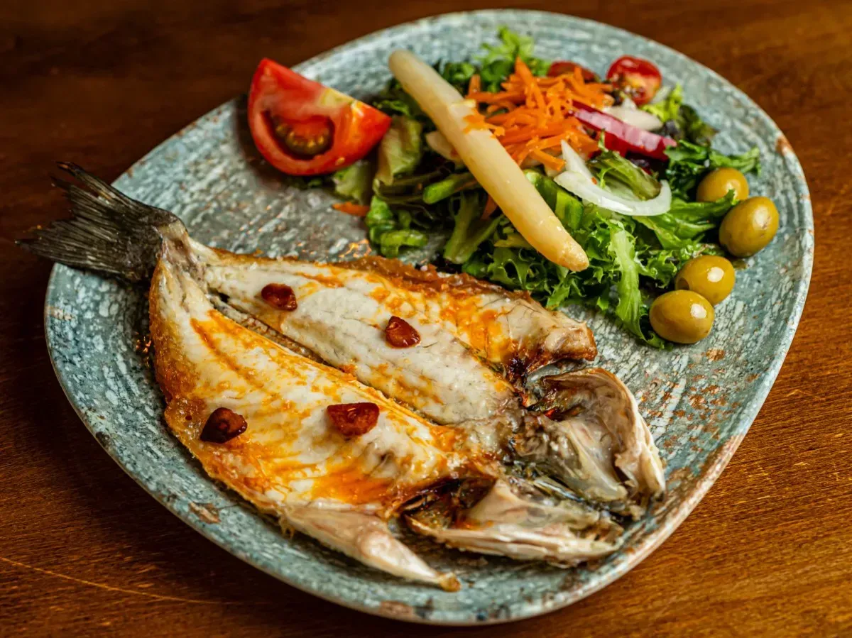 Un plato de pescado y verduras en una mesa de madera.