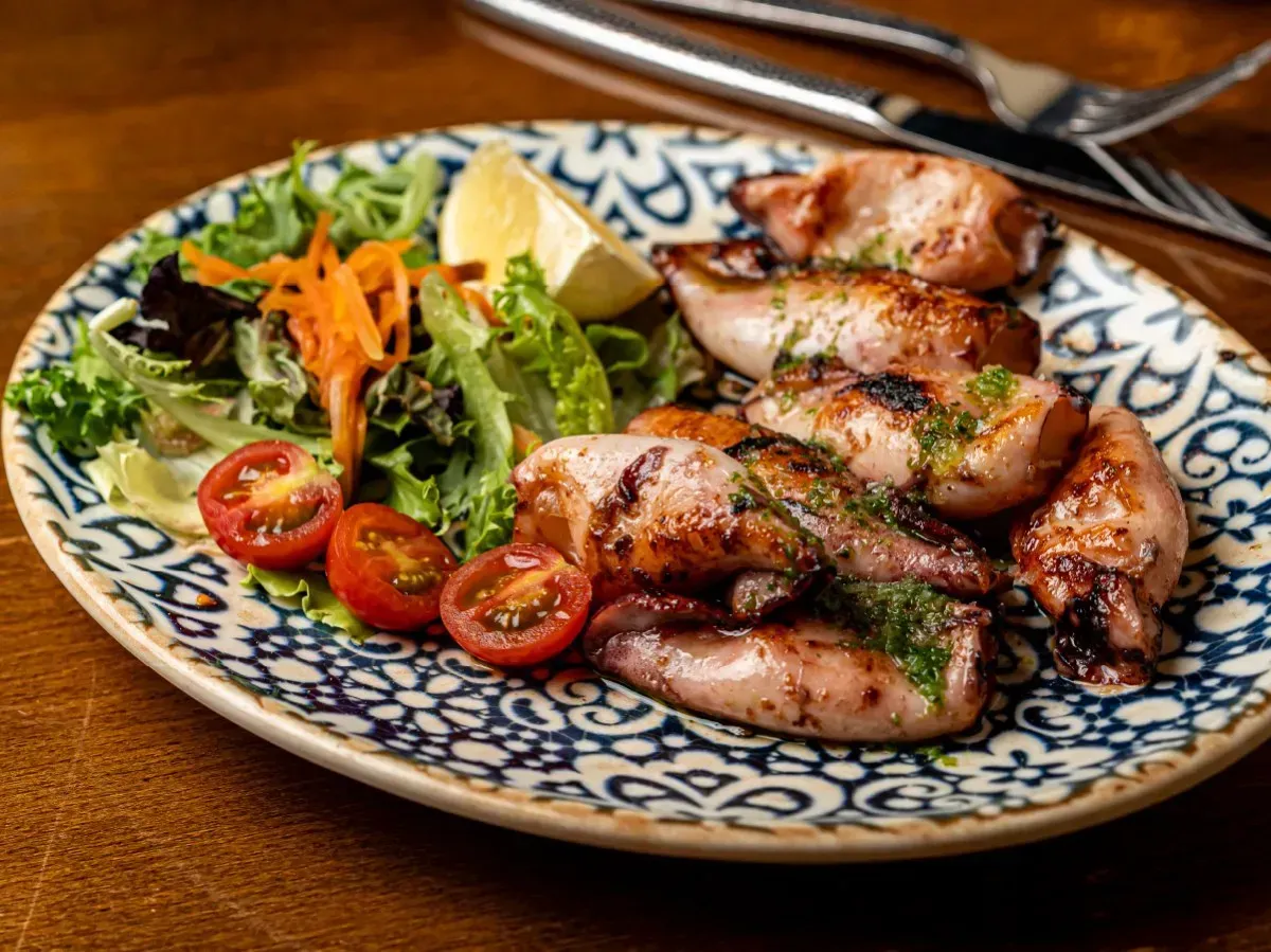 Un plato de comida con calamares y tomates en una mesa.