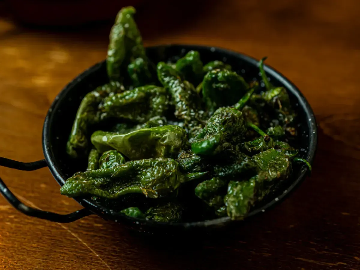 Un bol de pimientos verdes está sobre una mesa de madera.