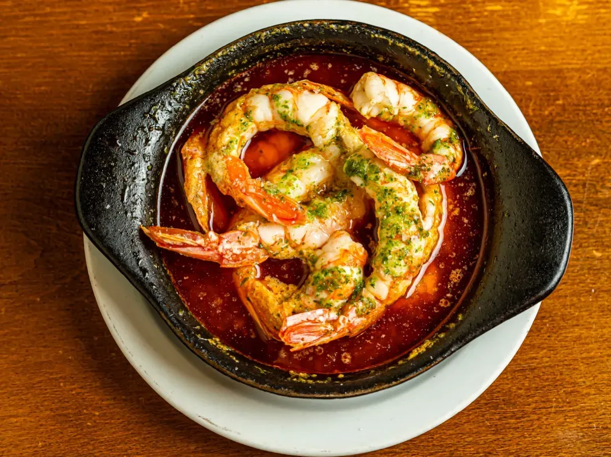 Un tazón de camarones está sobre un plato blanco sobre una mesa de madera.