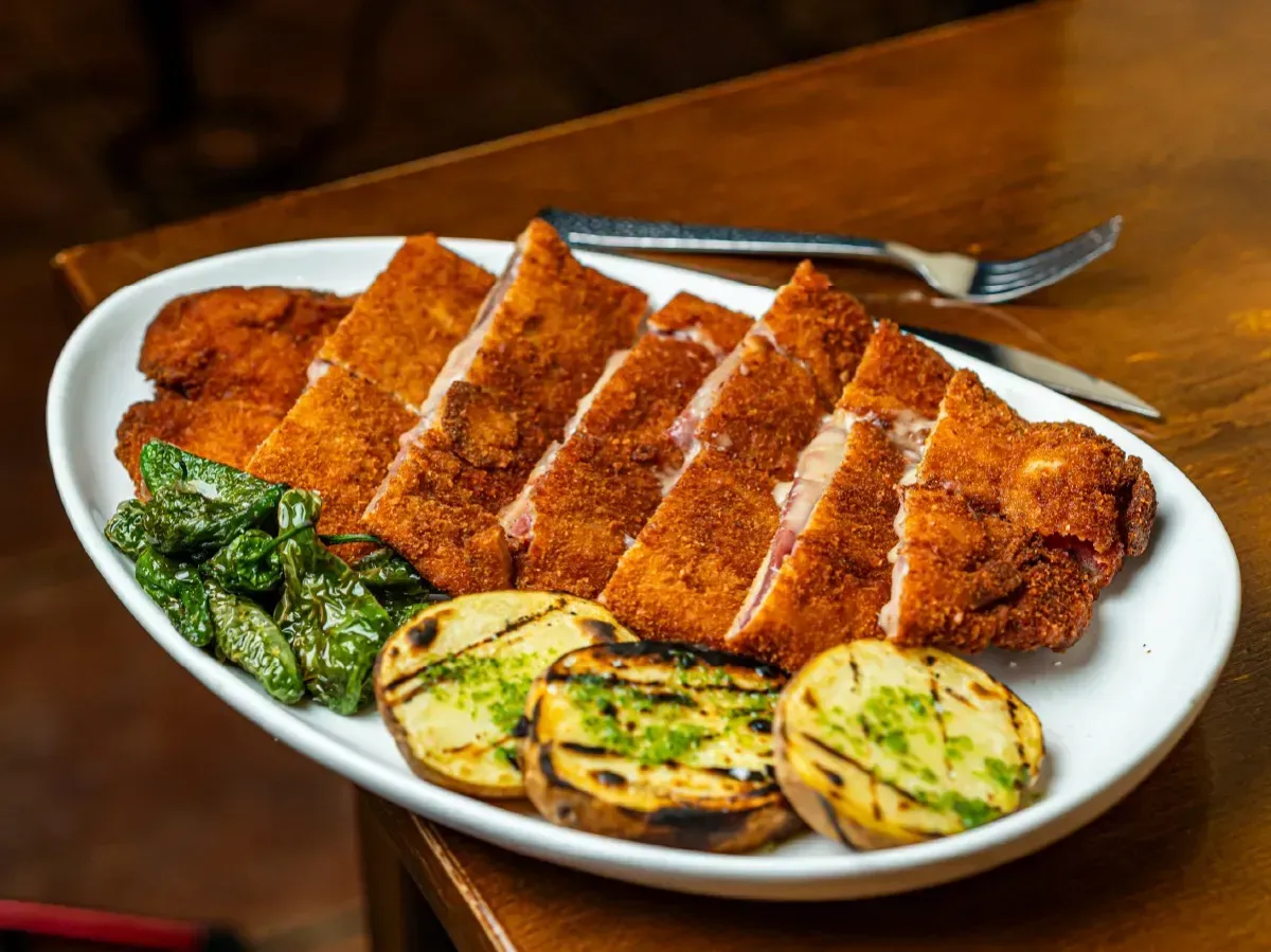 Un plato blanco cubierto con carne frita y patatas sobre una mesa de madera.