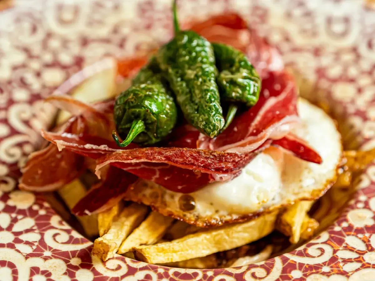 Un primer plano de un plato de comida con papas fritas, huevos, pimientos y jamón.