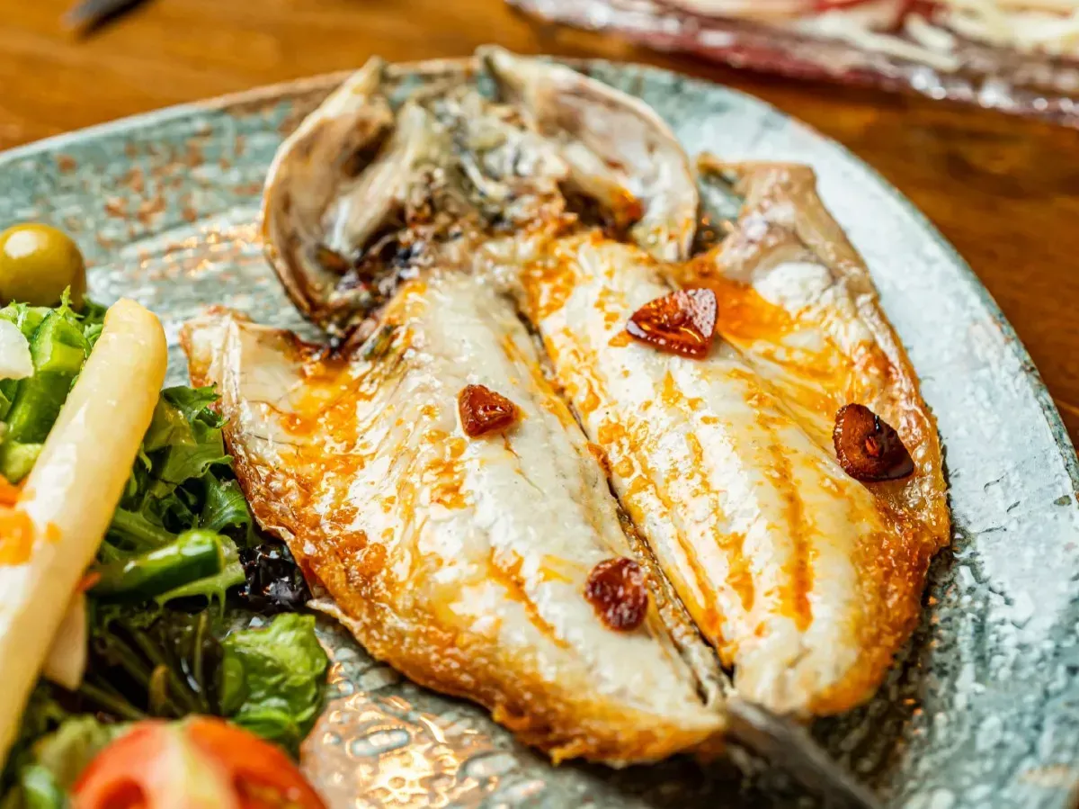 Un primer plano de un plato de comida con pescado y verduras sobre una mesa.
