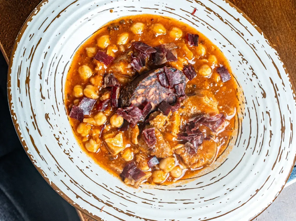 Un plato blanco cubierto con un guiso de carne y garbanzos sobre una mesa de madera.
