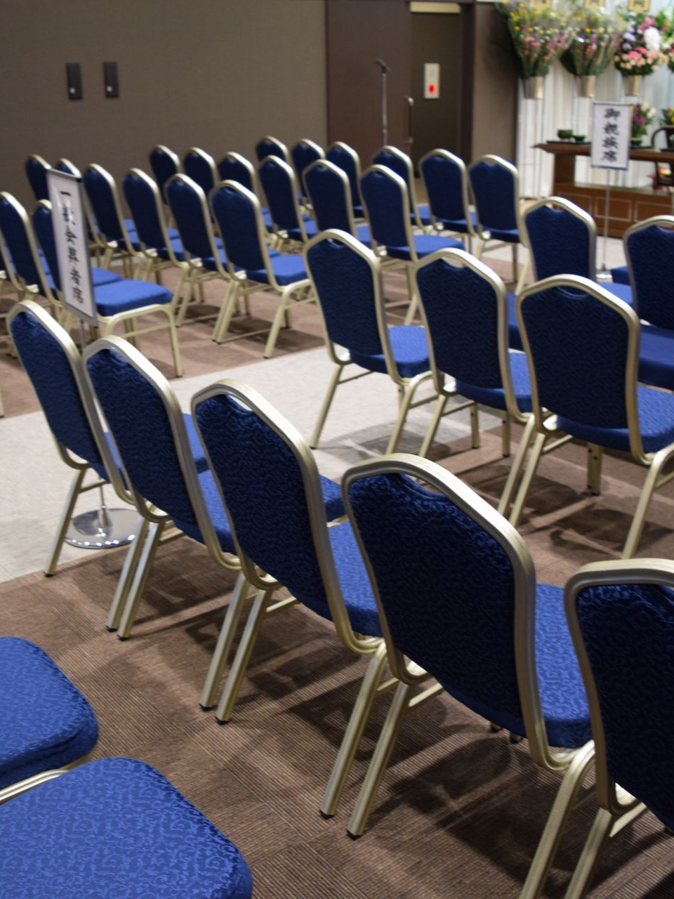 Des rangées de chaises bleues vides dans un hall pour des funérailles.