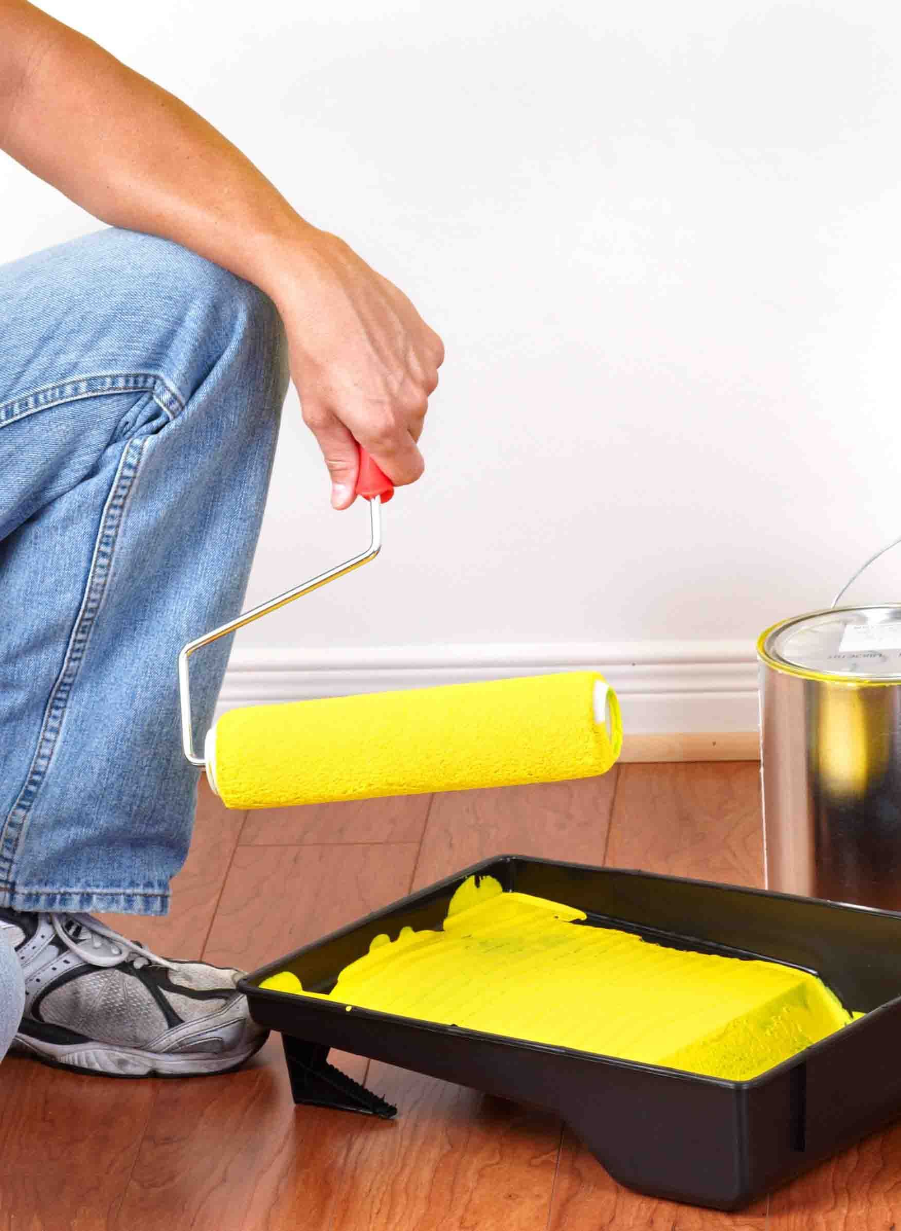 Una persona está usando un rodillo de pintura amarillo para pintar una pared.