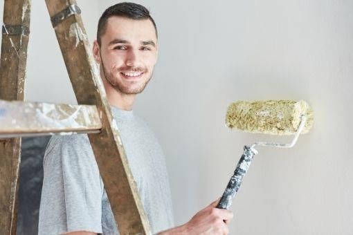 Ein Mann steht mit einer Farbrolle in der Hand neben einer Leiter.