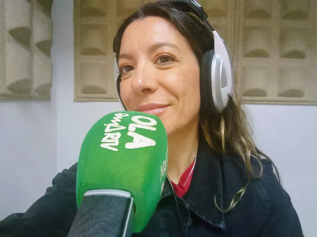 Mujer con auriculares sonriendo a un micrófono con el logo de 