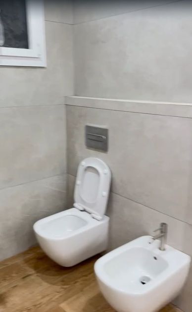 Baño minimalista con un inodoro y un bidé junto a una pared revestida de azulejos y una ventana.