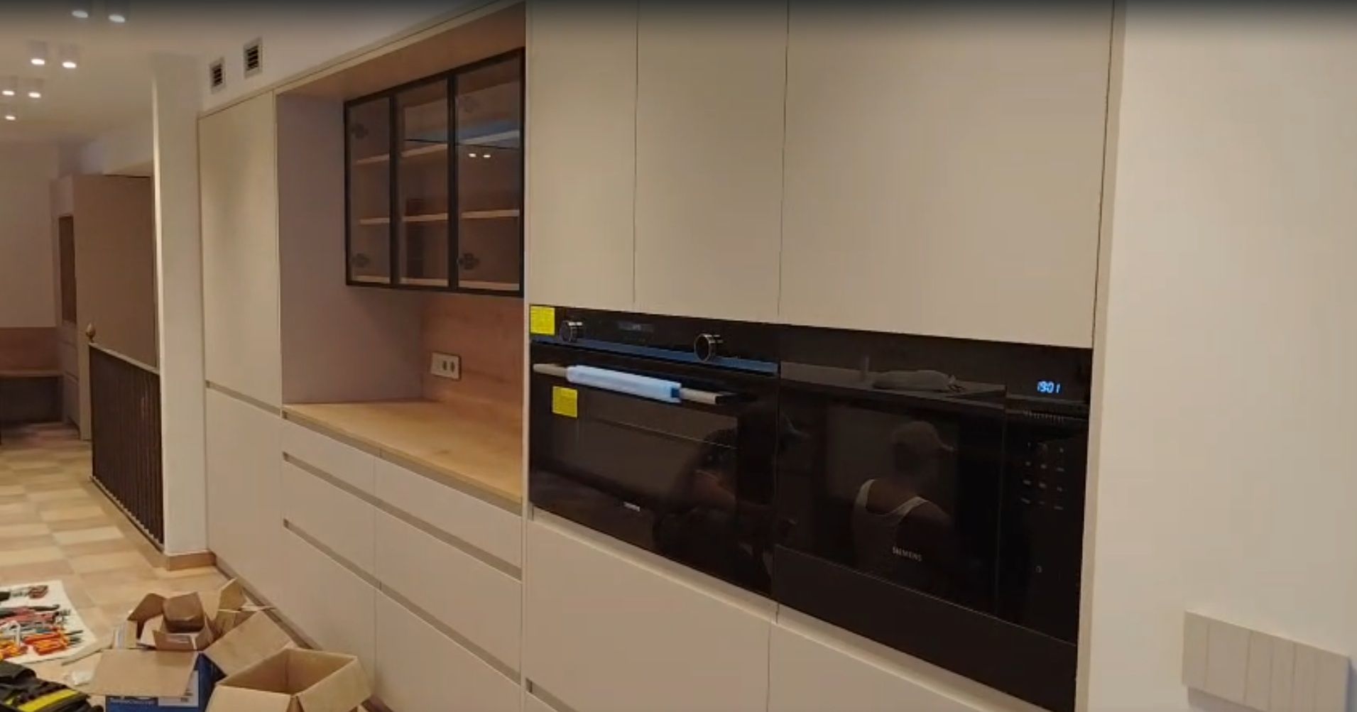 Cocina moderna con armarios blancos, horno negro empotrado y estanterías abiertas en construcción.