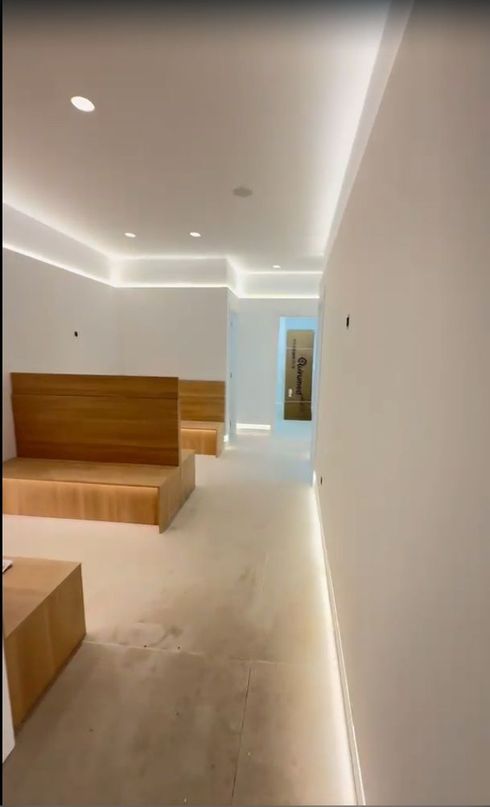 Habitación moderna y minimalista con bancos de madera, paredes blancas, iluminación empotrada y un pasillo estrecho
