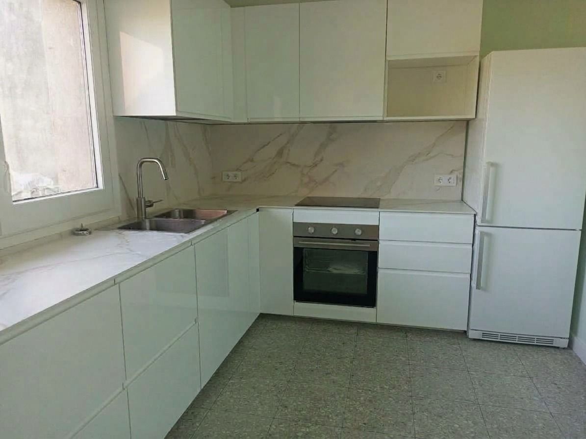 Cocina moderna blanca con armarios, fregadero, estufa y refrigerador sobre un suelo verde moteado