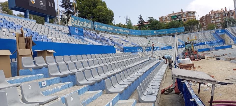 Gradas azules y grises vacías de un estadio junto al mar, al lado de una playa de arena